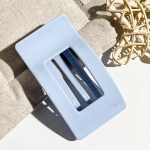 Detail view of a light blue rectangular hair claw clip with a hollow design on fabric