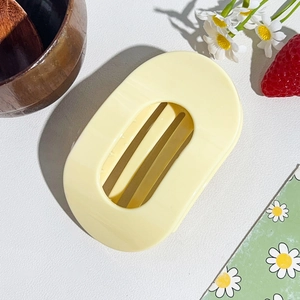 Detailed view of the large pale yellow oval hair claw clip set on a floral backdrop