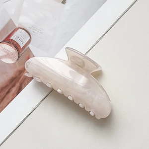 Détail de la pince à cheveux marbrée crème avec bordure de perles sur un fond de magazine