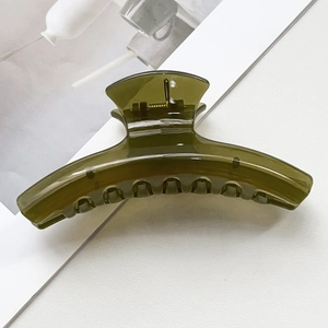 Détail d'une pince à cheveux vert olive translucide avec ressort sur cuir blanc