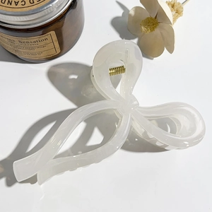 Detail of a cream white bow claw clip with cloud texture and gold metal spring