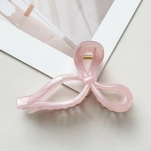 Détail macro d'une pince à cheveux en acétate rose pâle avec texture marbrée et ressort doré