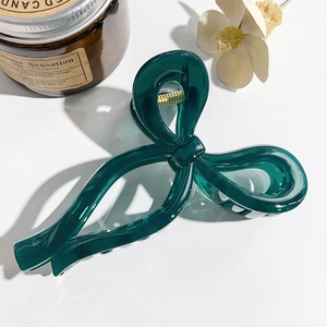 Detail of dark green resin bow hair claw clip showing glossy finish and gold metal spring
