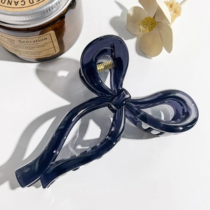 Detail view of a translucent purple bow hair claw clip with golden spring on a white desk