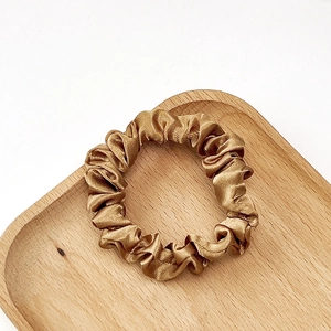 Detail of a golden satin scrunchie with pleated texture on a wooden tray