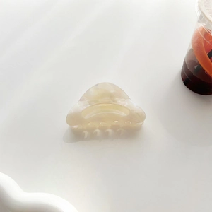 Détail d'une pince à cheveux triangulaire en acétate crème marbré dans un décor de vie épuré