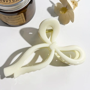 Detailed close-up of a creamy white bow-shaped hair claw clip with golden metal spring