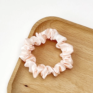 Macro detail of soft pink satin scrunchie with silky folds and elegant texture
