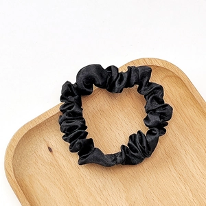 Close-up of a black satin scrunchie on a heart-shaped wooden tray with elegant folds