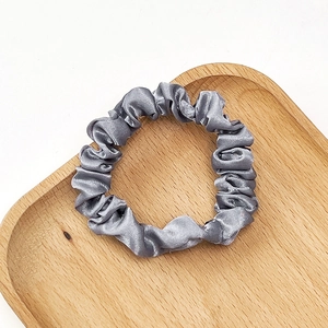 Detailed close-up of a grey pleated satin scrunchie on a wooden tray with a white backdrop