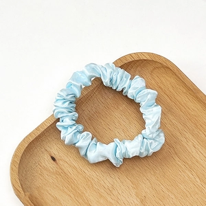 Close-up of light blue pleated satin scrunchie on a decorative wooden tray