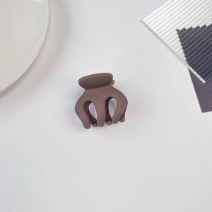 Détail macro d'une pince à cheveux mate marron foncé sur fond blanc minimaliste