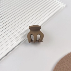 Détail macro d'une petite pince à cheveux mate marron café sur une surface blanche épurée