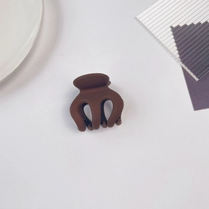 Gros plan d'une mini pince à cheveux marron mat sur fond de céramique minimaliste