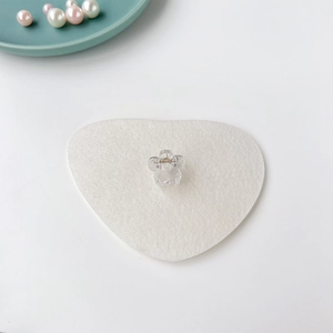 Gros plan d'une mini pince à cheveux fleur transparente sur un fond en feutre blanc en cœur