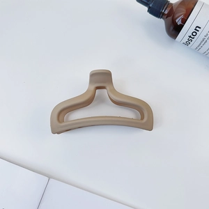 Macro shot of large matte cream hair claw clip with cutout fishtail design on white desk