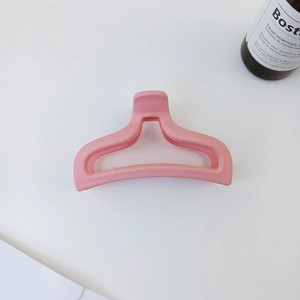 Close-up of pink matte fishtail hair claw clip with hollow design on white surface