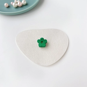 Gros plan d'une mini pince à cheveux fleur verte mate sur un tapis en feutre blanc