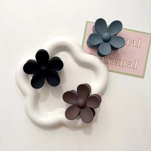 Close-up of matte finish flower hair clips in black, blue, and brown on a white plate
