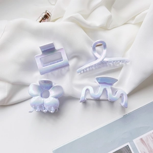 Macro view of four iridescent claw clips in geometric shapes on soft white fabric