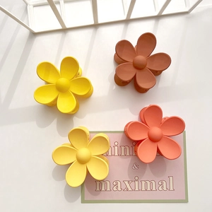 Detail view of four matte flower hair claws in yellow, orange, and brown tones