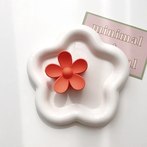 Macro view of matte orange floral hair claw clip on white decorative floral tray