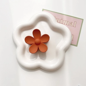 Detail of matte orange flower hair claw clip on white ceramic tray with minimal aesthetic