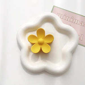 Close-up of a matte yellow five-petal flower hair claw clip on a white ceramic tray
