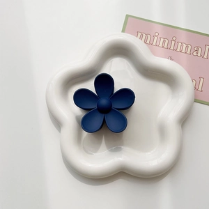 Close-up of matte dark blue flower hair claw clip on a white ceramic petal tray