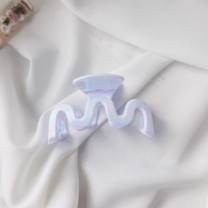 Detail of iridescent wavy shark hair claw clip on soft white silk fabric background