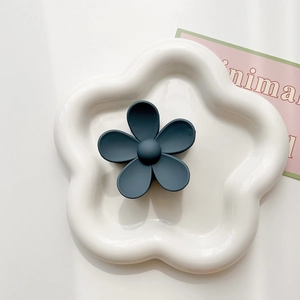 Macro shot of a matte dark teal five-petal flower hair claw on a white ceramic tray