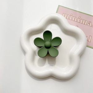 Detailed macro view of a matte forest green flower hair claw clip on a ceramic tray
