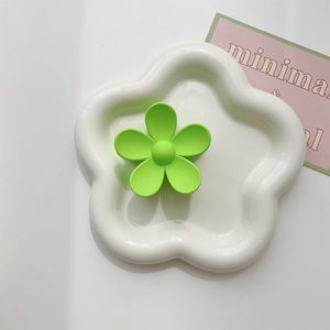 Macro shot of a matte neon green flower hair claw on a white ceramic decorative plate