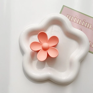 Macro detail of a coral orange matte flower hair claw on a white ceramic display tray