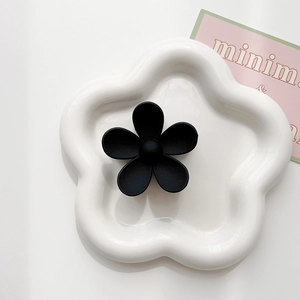 Close-up of matte black flower hair claw clip with minimalist floral design on white tray