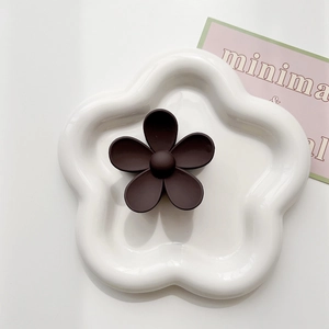 Detailed macro view of a matte dark brown flower hair claw clip on a white plate