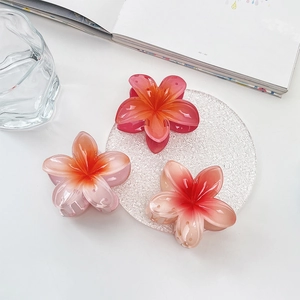 Detailed top view of three glossy frangipani flower hair claws in vibrant pink and orange