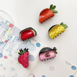 Detailed view of colorful acrylic fruit hair claws including carrot and strawberry designs