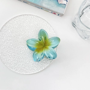 Detail of gradient blue and green plumeria hair claw clip on a white textured dish
