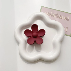 Detail view of a matte dark red flower hair claw clip on a white ceramic tray