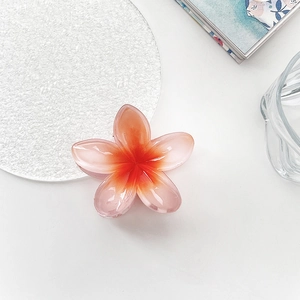 Detail of tropical frangipani hair claw clip with orange pink gradient and glossy finish