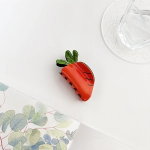 Macro detail of a cute carrot shaped acrylic hair claw clip with vibrant orange and green finish