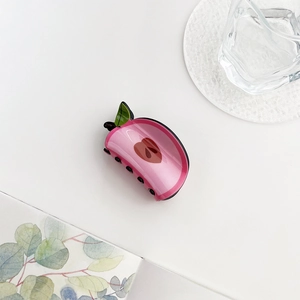 Detail of pink acrylic apple hair claw clip with leaf accent on a minimalist background