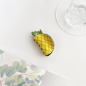 Close-up of a cute yellow pineapple-shaped hair claw clip on a stylish summer background