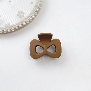 Close-up of a matte brown bow-shaped claw clip on an elegant lace background