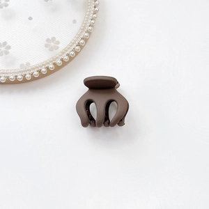 Close-up of matte brown mini hair claw clip for ponytail on a white floral background