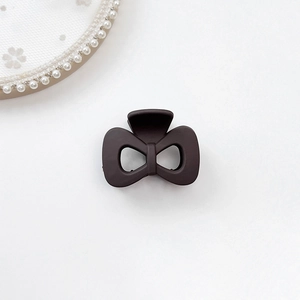 Detail of a matte brown bow-shaped hair claw clip on white lace and pearl background
