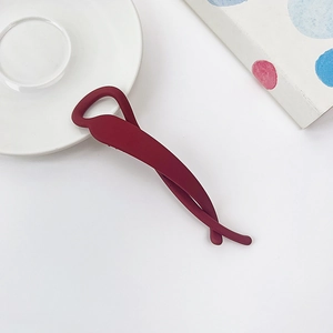Détail d'une pince banane mate bordeaux au design torsadé sur une assiette blanche