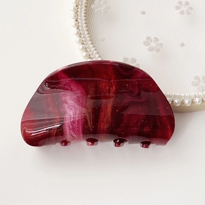 Detail of burgundy marble acetate hair claw clip with glossy shimmering texture