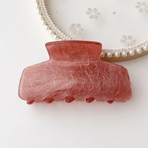 Close-up of translucent red acetate hair claw with textured silk pattern on white lace